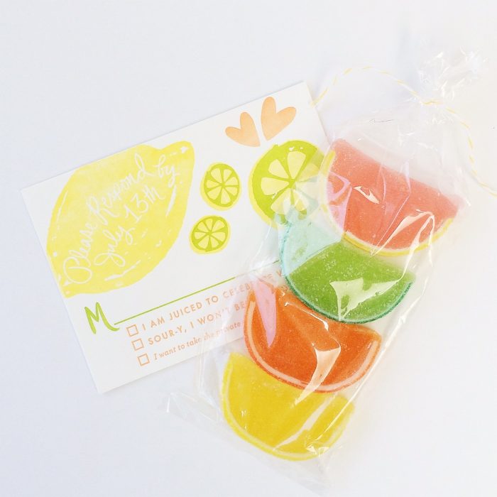 Clear bag with citrus gummies in it next to an invitation to a bridal shower. 