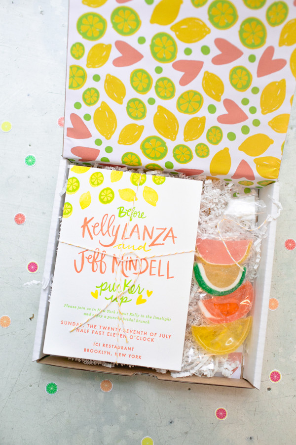 Overhead shot of a citrus designed box with a bridal shower invitation inside with citrus candies. 