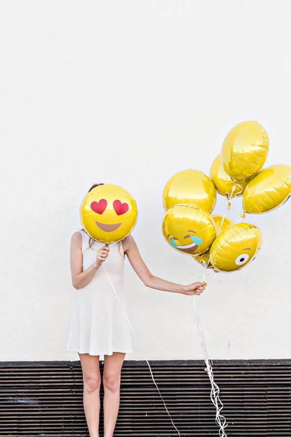 A person wearing a costume, with Emoji Balloons