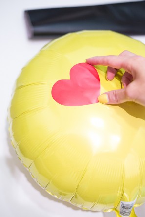 hand placing heart on emoji balloon