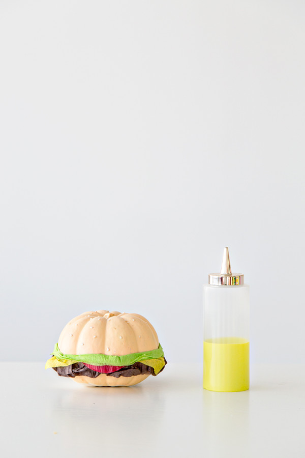 A fake burger and a bottle of yellow liquid 