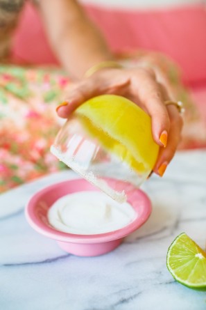 Someone holding a cup with an orange drink in it over a bowl 