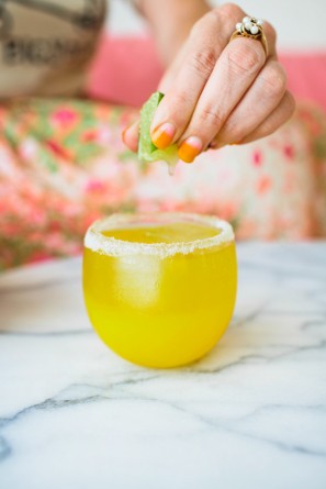 A person squeezing a lime into an orange drink