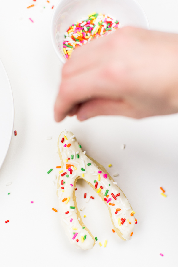 Someone putting sprinkles on a donut