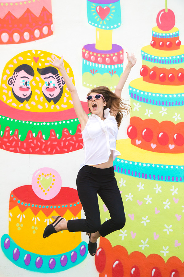 A woman in front of a mural with cakes and faces 