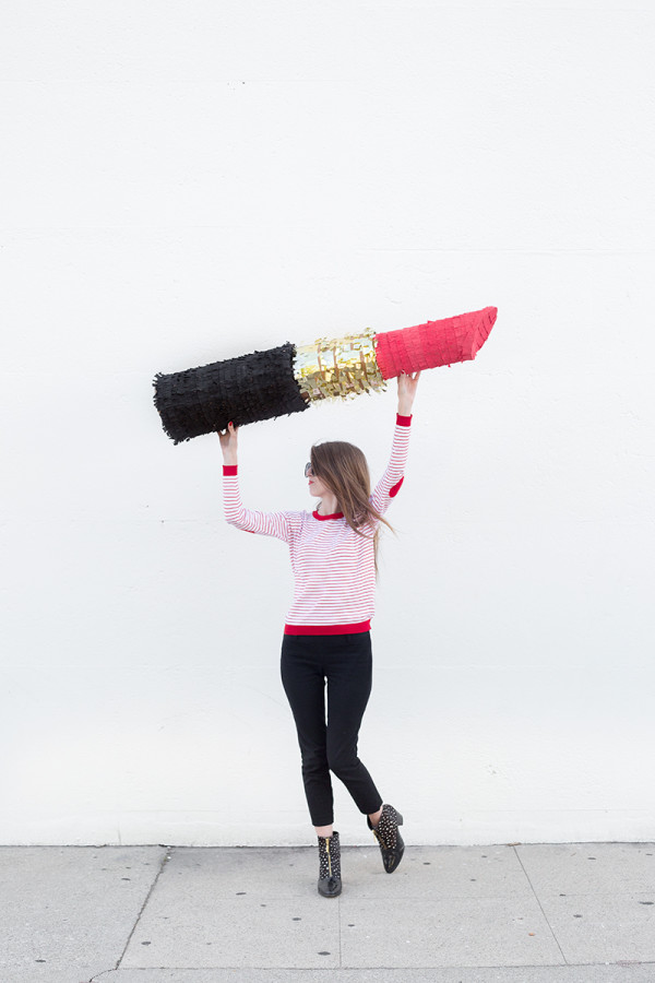 A woman holding a big lipstick piñata 