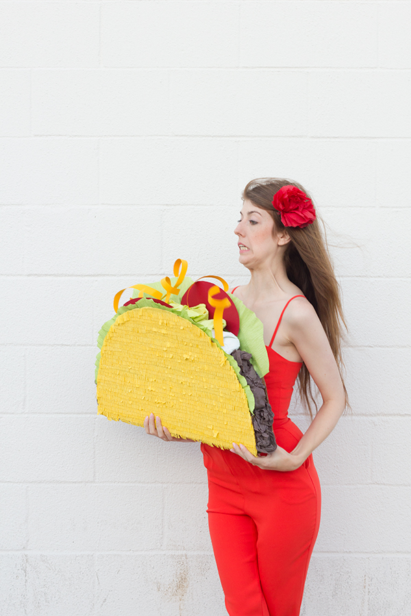 A woman wearing a red dress and holding a taco piñata 