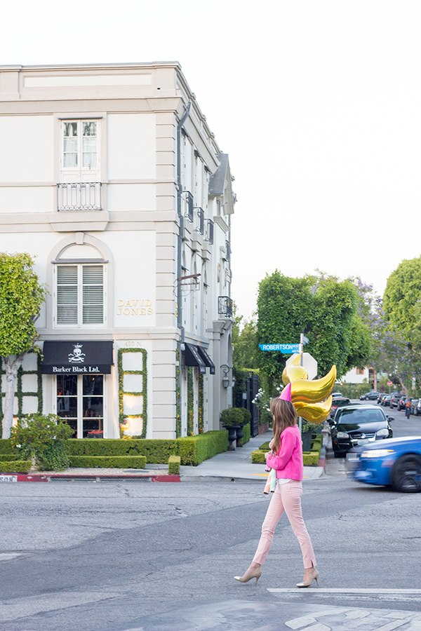 A woman holding a gold balloon walking across a street