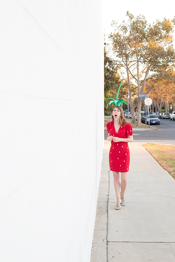 A woman in a strawberry costume walking on the side walk 