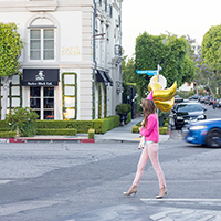 A woman holding a gold balloon walking down the street 
