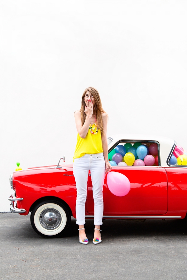 A woman standing next to a red car with balloons in it