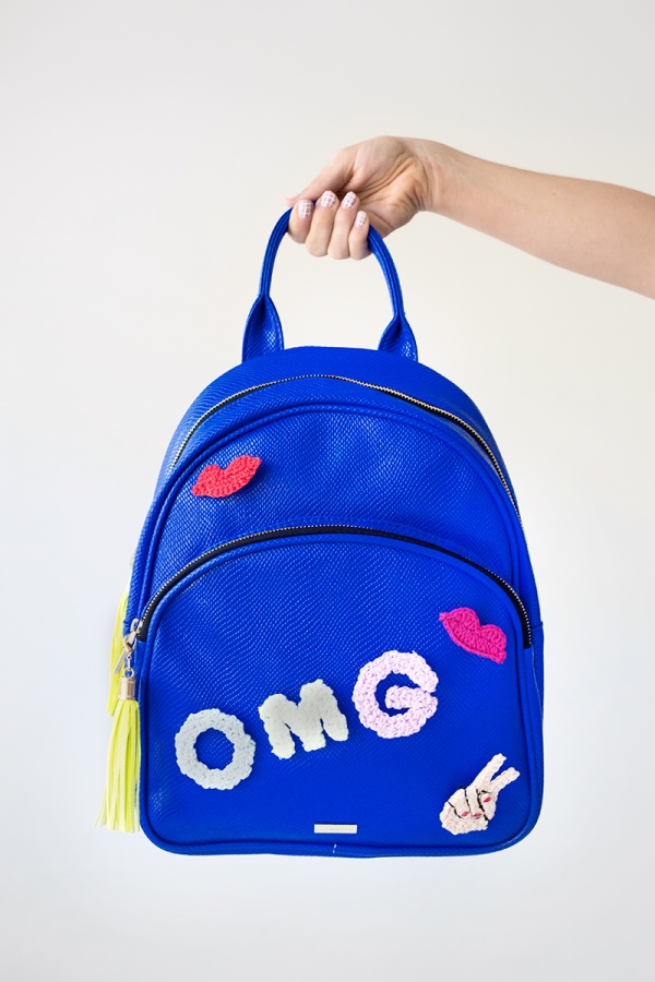 Someone holding a blue backpack that says \"omg\"
