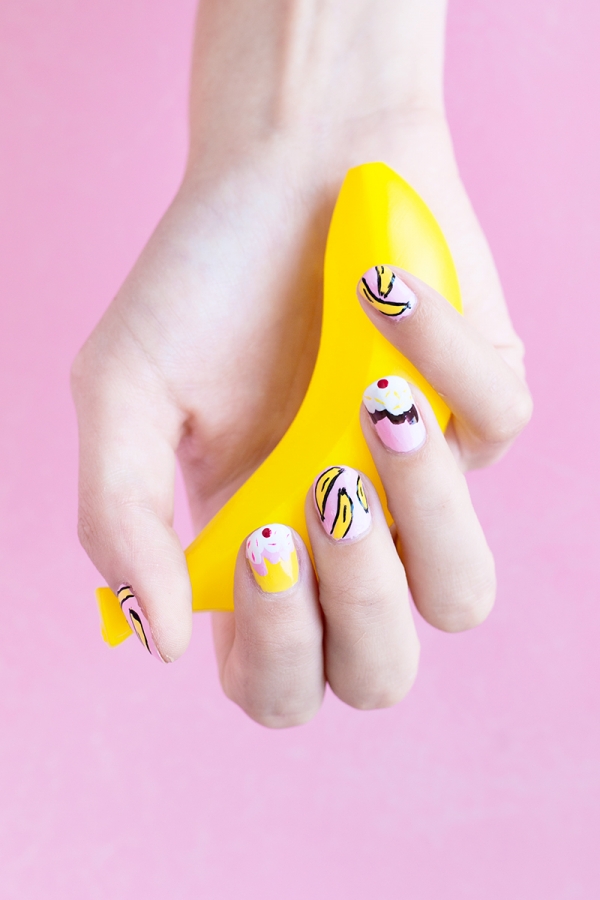 Someone with pink and yellow nails holding a fake banana 