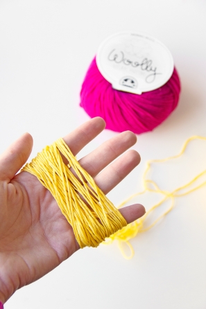 Someone holding yellow string and purple yarn