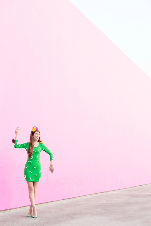 A woman wearing a cactus costume in front of a pink wall