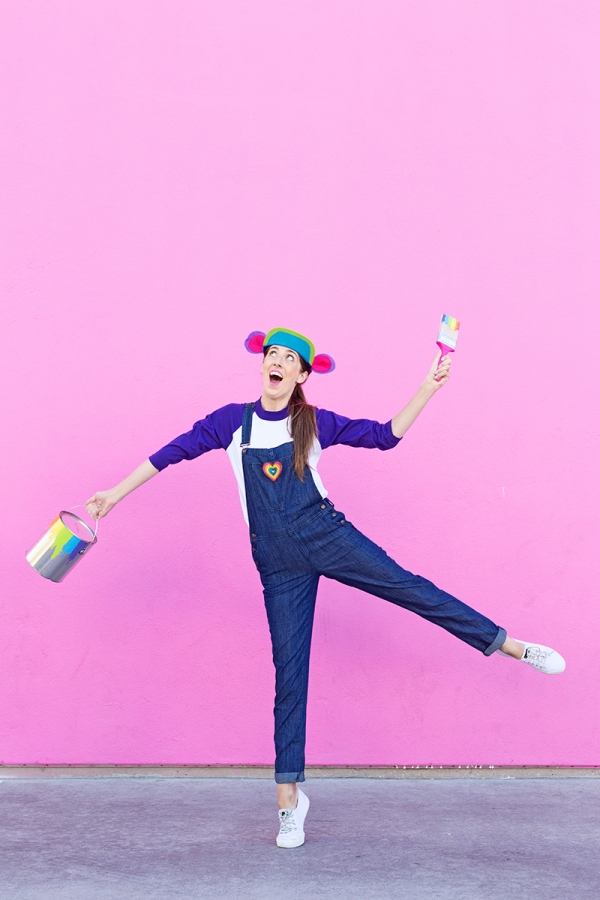 A woman in overalls in front of a pink wall