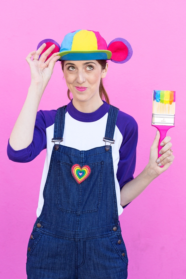 A woman wearing overalls and holding a rainbow paint brush