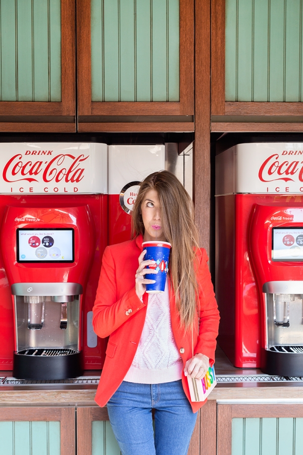 A woman standing in front of a coke machine, drinking a coke