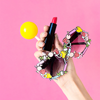 Someone holding glasses, lipstick, and a yellow ball