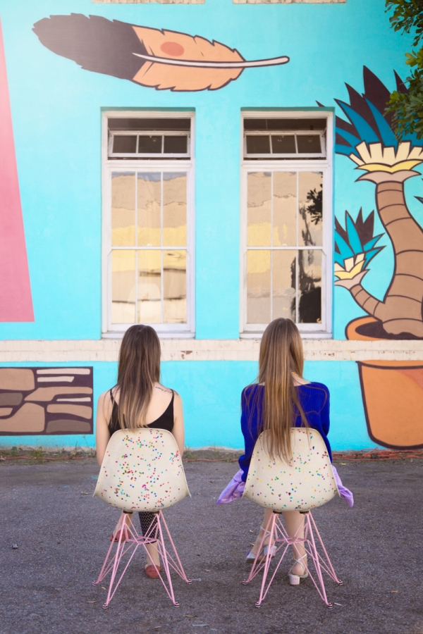 Two girls sitting in front of a mural