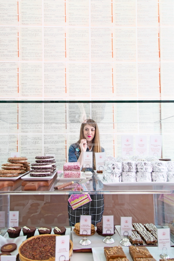 A woman standing behind a class container of desserts