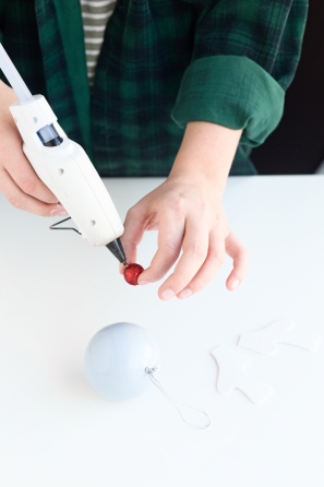 Someone gluing a red ball on a purple ornament 