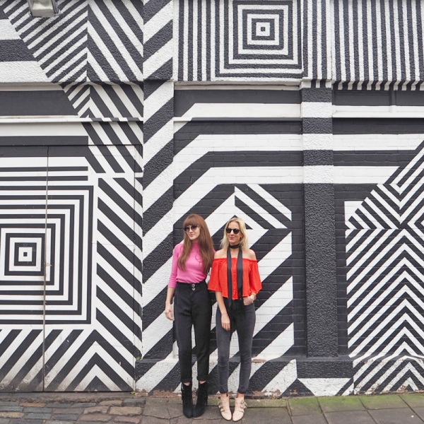 Two girls standing in front of a black and white patterned wall