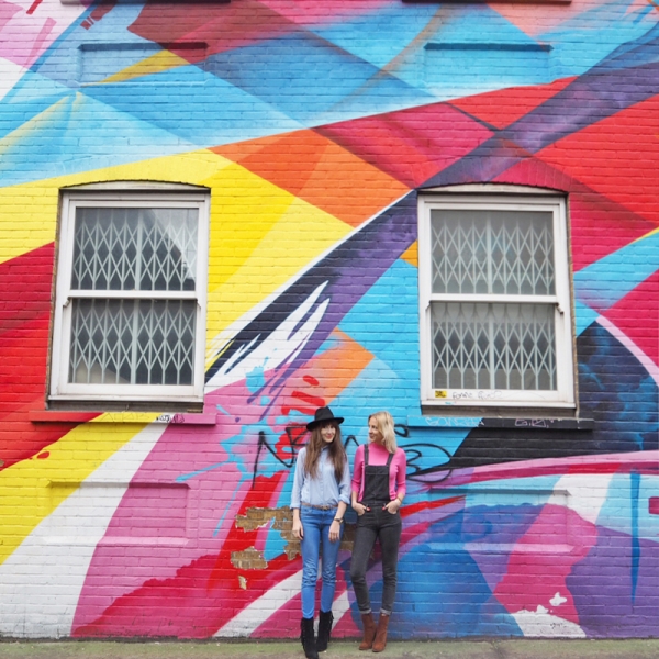 Two people standing in front of a colorful mural