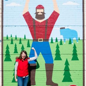 A woman standing in front of a lumberjack mural