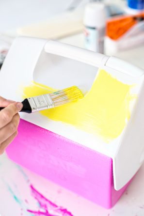 Someone painting a cooler yellow and pink