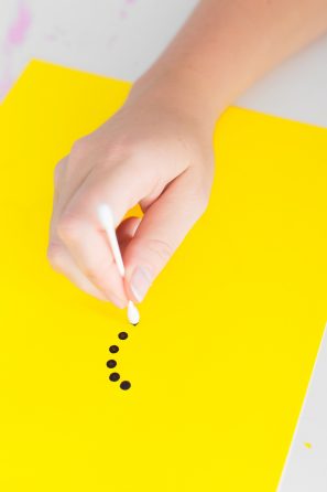 Someone putting black dots on a yellow paper