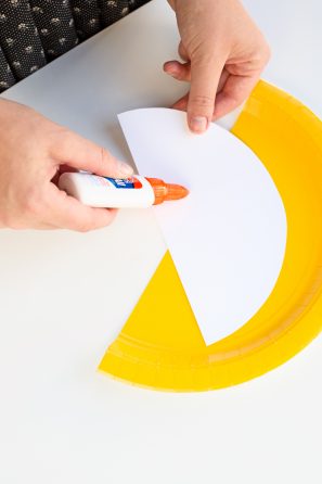 Someone gluing white paper on a yellow plate