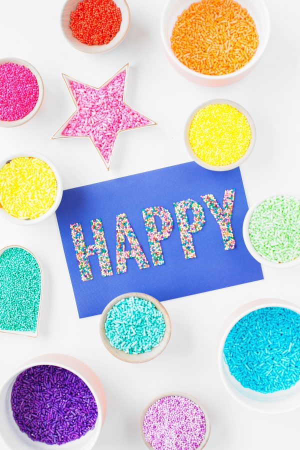 Containers with sprinkles and a paper that says \"happy\"