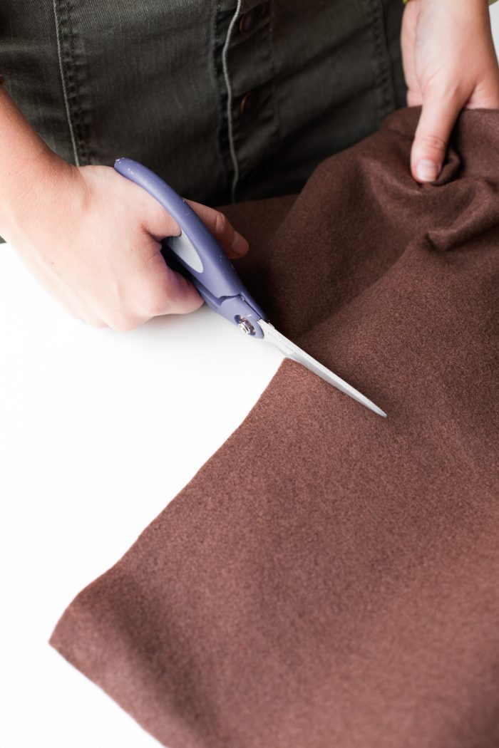 Someone cutting brown fabric with scissors 