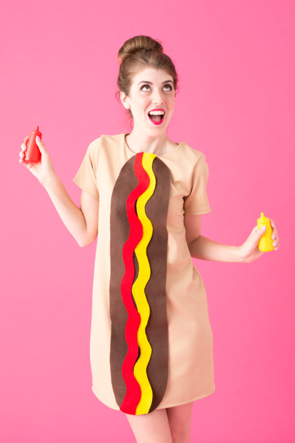 A woman dressed up as a hot dog holding a bottle of ketchup and a bottle of mustard. 