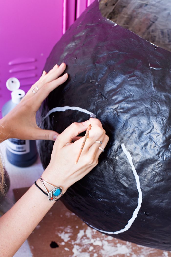 Someone painting white on a black newspaper ball