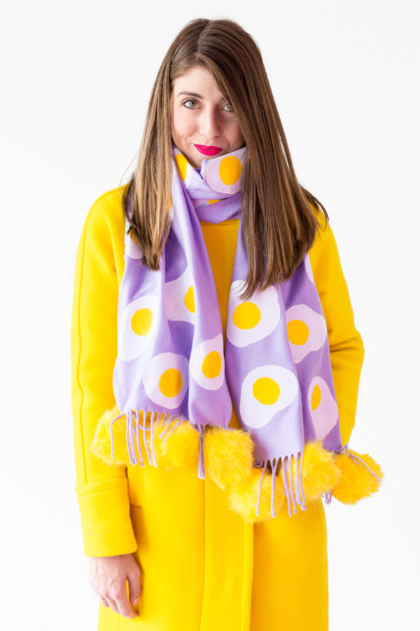 A woman wearing a purple scarf with eggs on it and a yellow jacket