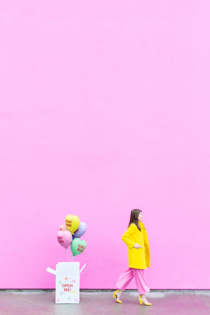 A woman and balloons in front of a pink wall