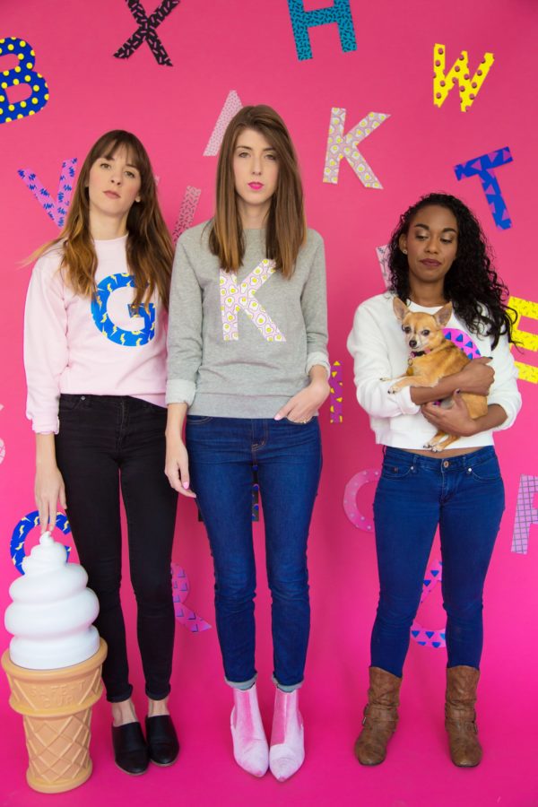 Three girls wearing sweaters in front of a pink wall