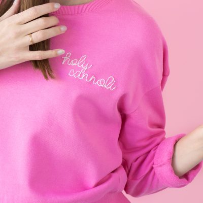 The corner of a pink crew neck with embroidered words on it