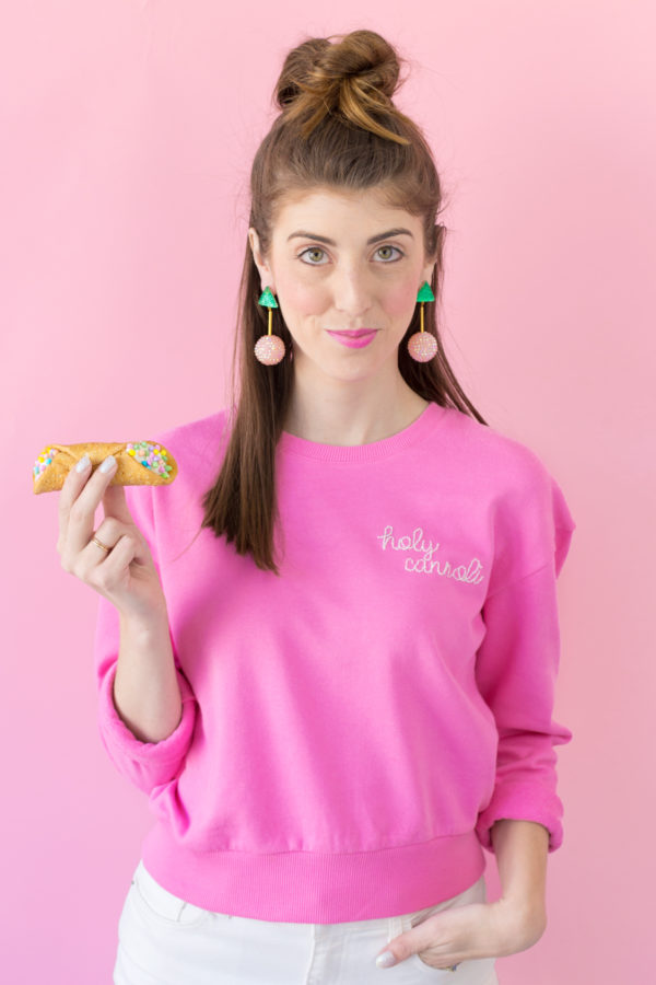 A woman in a pink crewneck holding a cannoli 