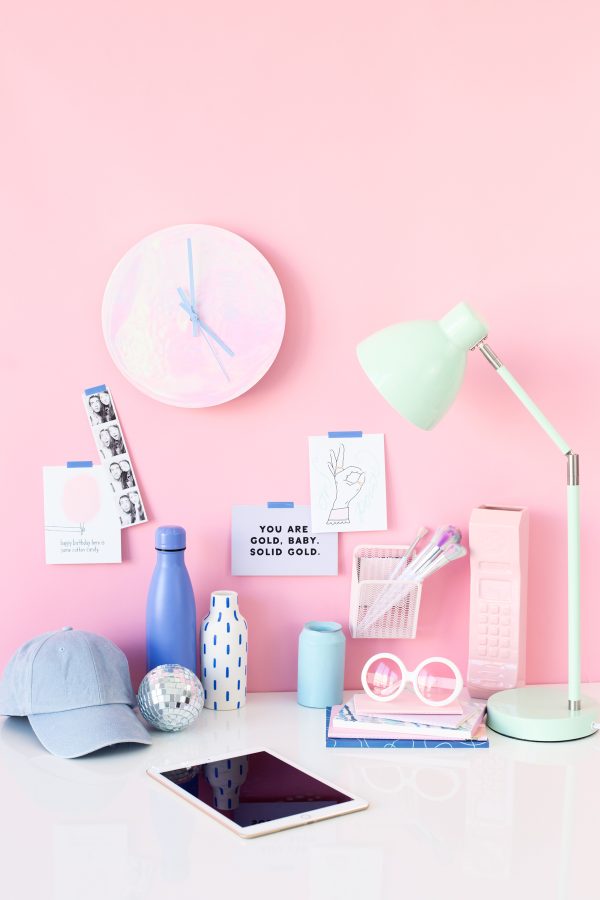 A bunch of items sitting on a desk in front of a pink wall