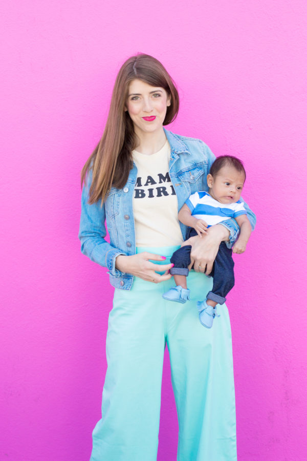 A woman holding a baby in front of a pink wall