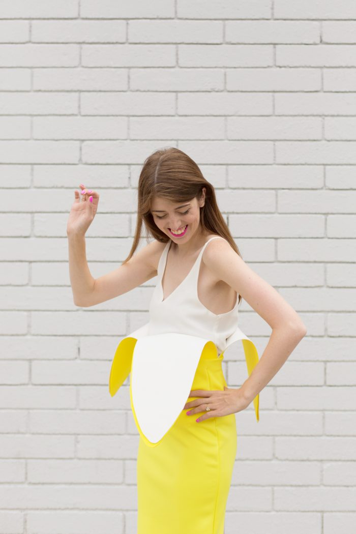 A woman standing next to a brick wall, with Banana Costume