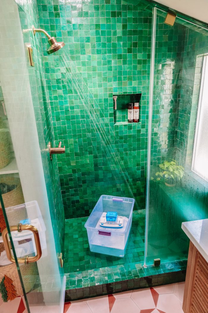A green tiled shower with a soap bucket