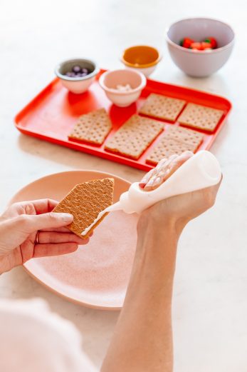 Someone putting frosting on a house shaped graham cracker