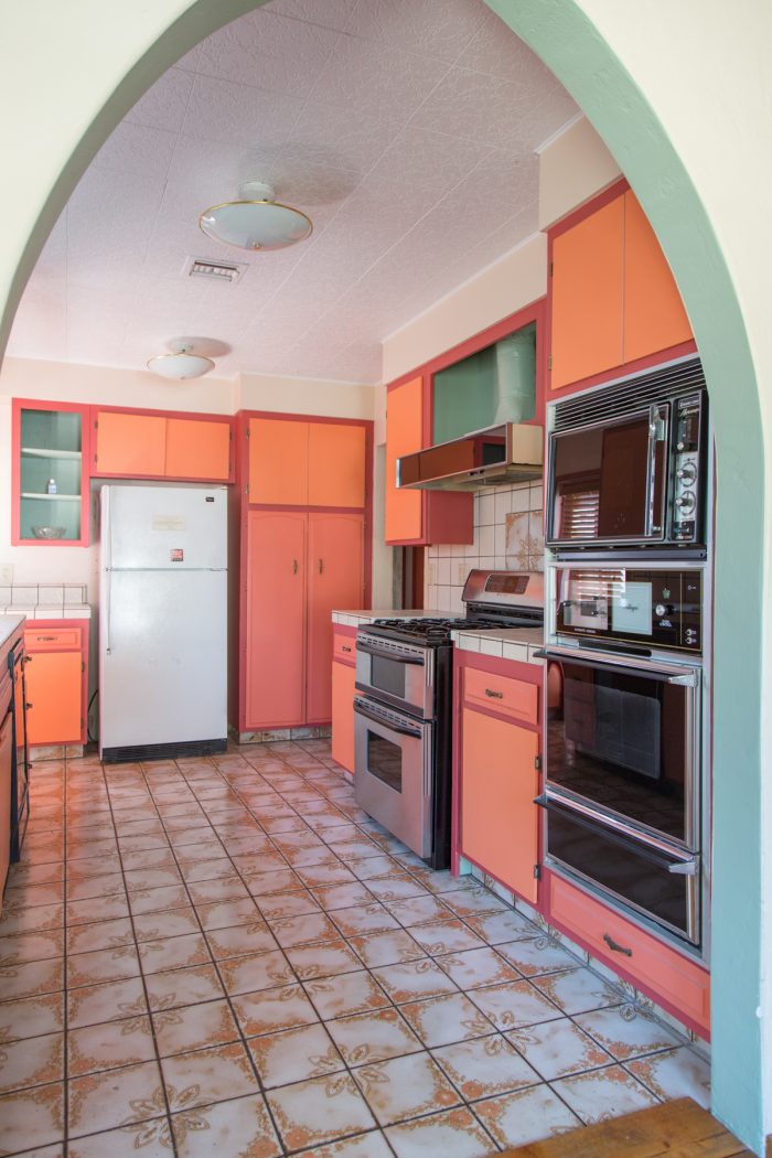 A kitchen with a fridge, stove, oven, microwave and orange cabinets