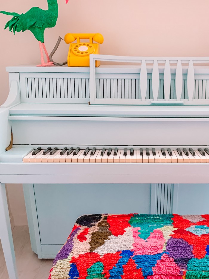 Blue painted piano with a colorful bench and a yellow phone on top