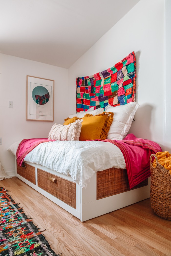 Rattan IKEA daybed with pillows on top and a rug hanging behind it