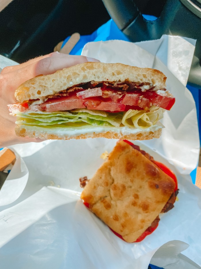 BLT sandwich on white paper on someone's lap